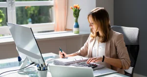 Female accountant working at desk with computer, calculator, and financial documents, representing answers to questions about the 2011 CPA exam