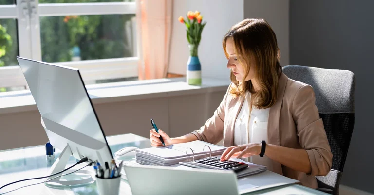 Female accountant working at desk with computer, calculator, and financial documents, representing answers to questions about the 2011 CPA exam
