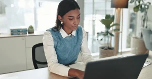 Woman working on a laptop in a bright office setting, representing 2014 CPA exam updates.