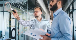 Two professionals brainstorming with charts on a glass wall — illustrating how to use Jedi mind tricks to pass the CPA exam through visualization and focus techniques.