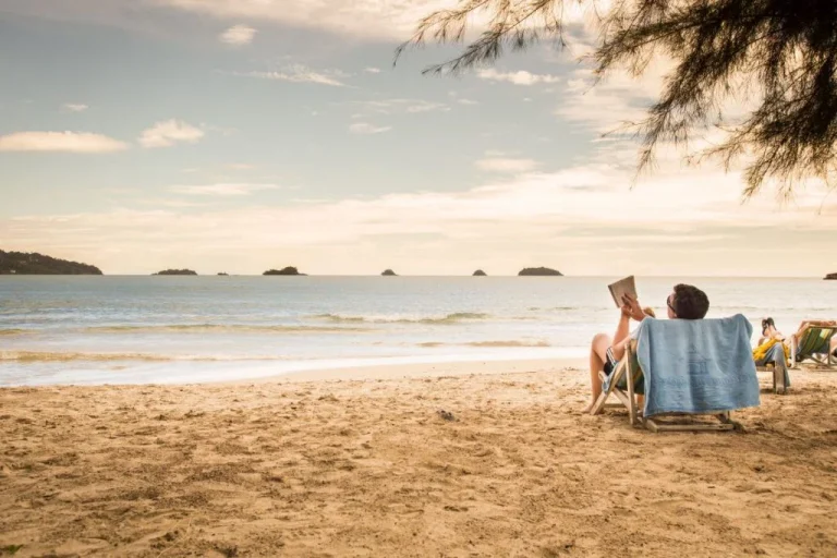 A person relaxing on a beach chair and reading a book–symbolizing how to study for the CPA exam while on vacation.