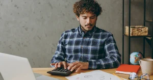 Young professional using a calculator at a desk with documents and a laptop, representing why you should work government