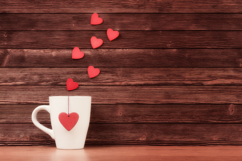 White cup with heart shapes over vintage wooden background