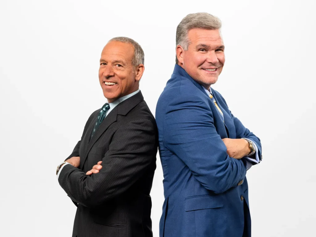 Roger Philipp and Peter Olinto stand back to back with their arms crossed.