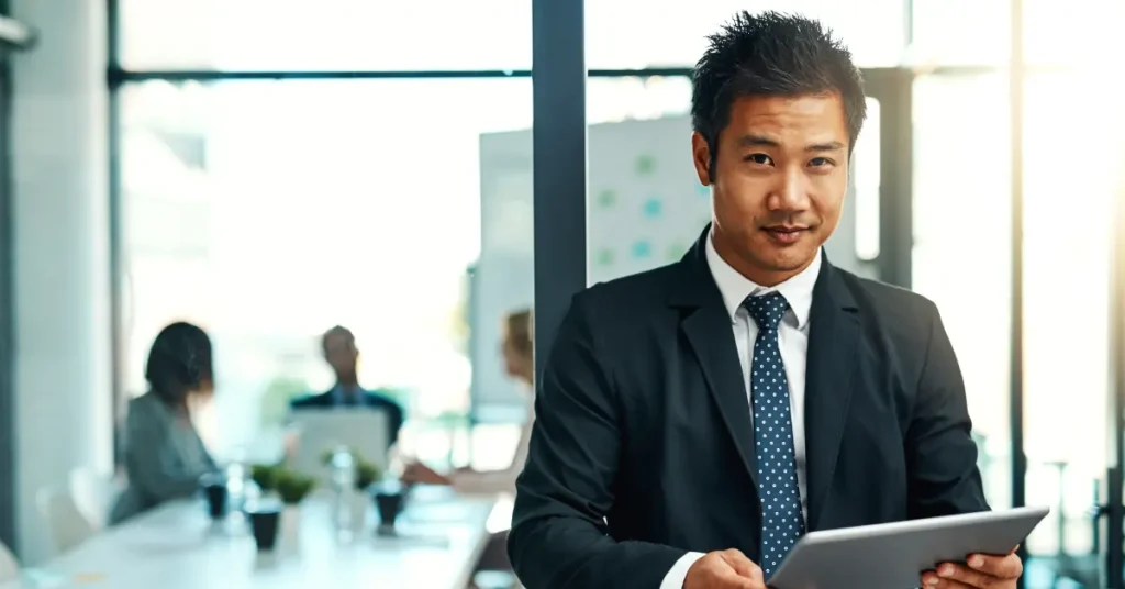 CMA professional holding a tablet and standing in front of a conference room full of colleagues.