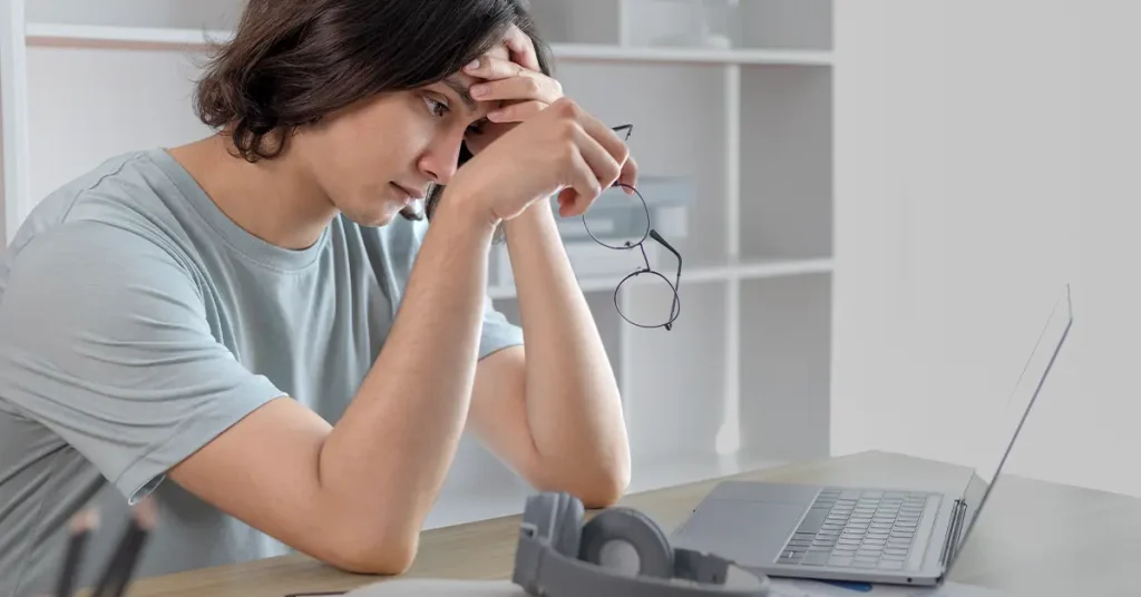 Frustrated student holding head and glasses looking at laptop